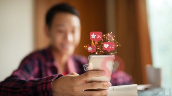 A Person Holding A Smartphone, Surrounded By Social Media Engagement Icons Showing Likes, Stars, And Comments, Suggesting A Social Media Strategy That Works.